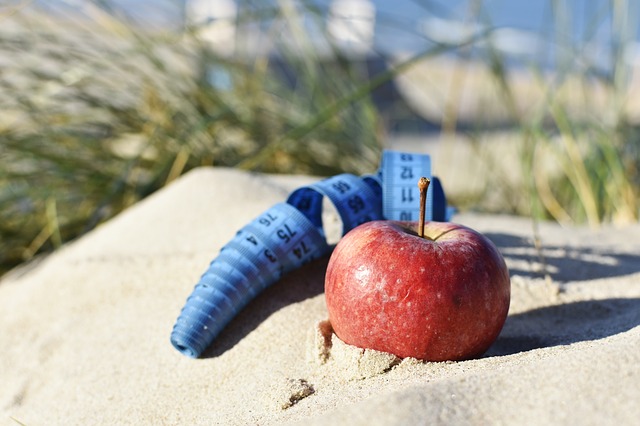 jablko v písku a stočený modrý metr